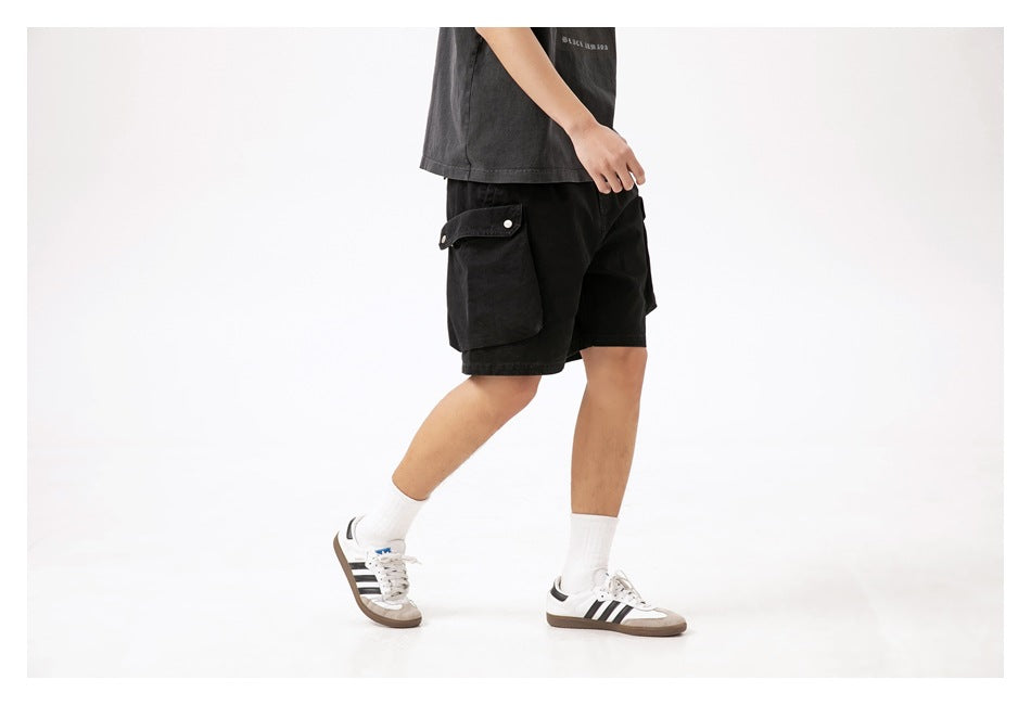 Side view of a model wearing black cargo shorts with a large snap-flap cargo pocket.