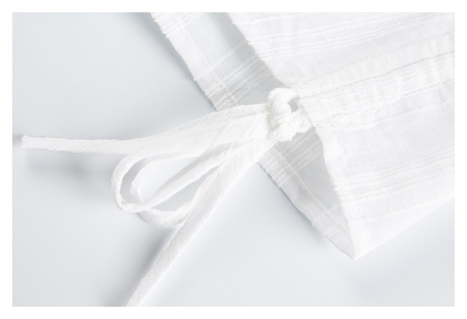 Close-up of a white garment tie knotted at the side, against raised stripe-textured fabric.