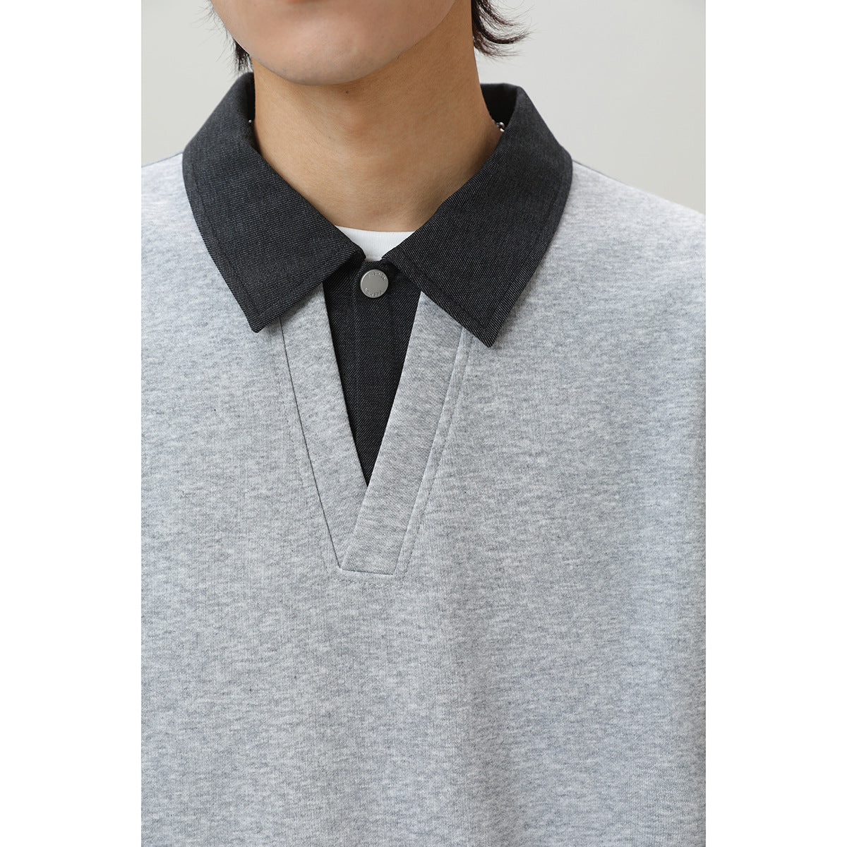 Close-up of a person wearing a light gray top with a dark charcoal collar and buttoned placket.