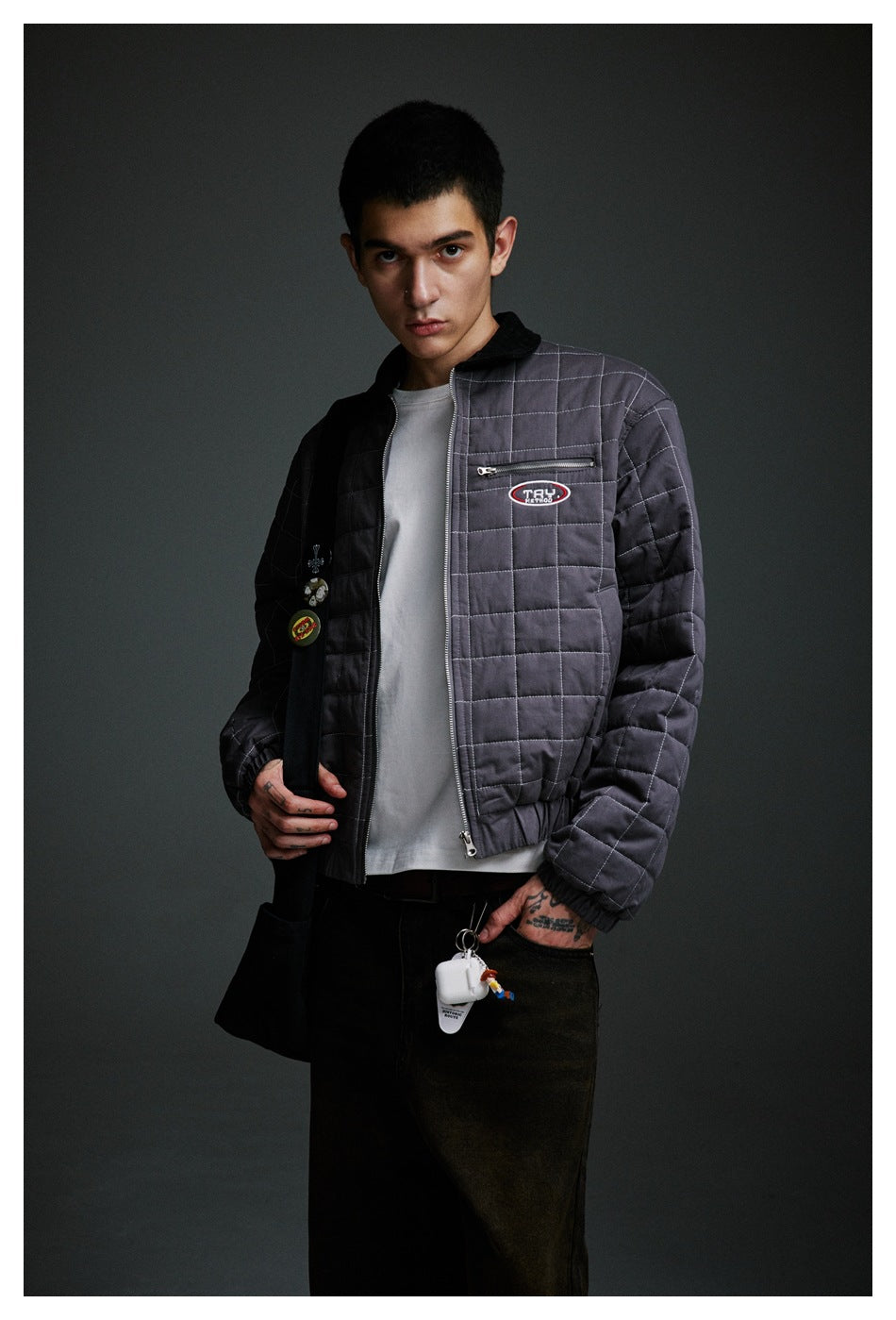 Closer front view of a model in an open charcoal-gray quilted jacket with a black collar and zip chest pocket.