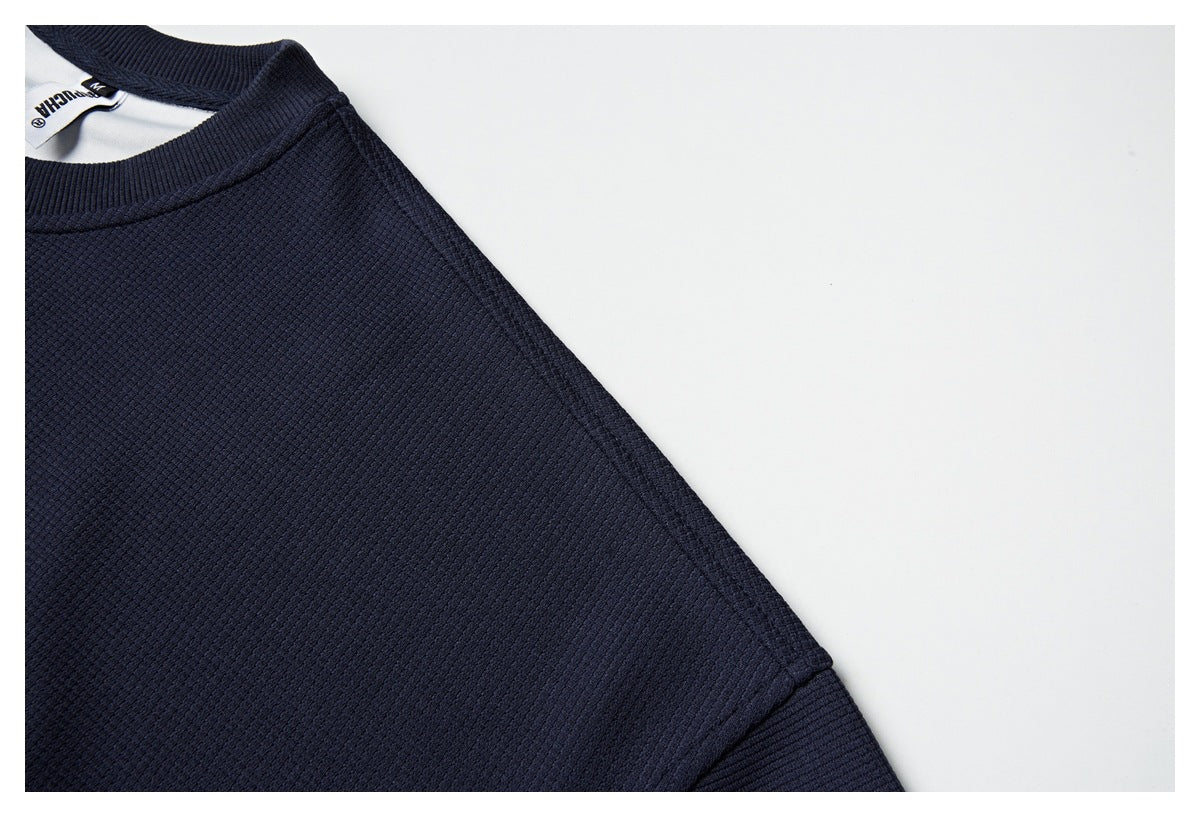 Close-up of the navy sweatshirt's textured shoulder and sleeve seam, with part of the neck label visible.
