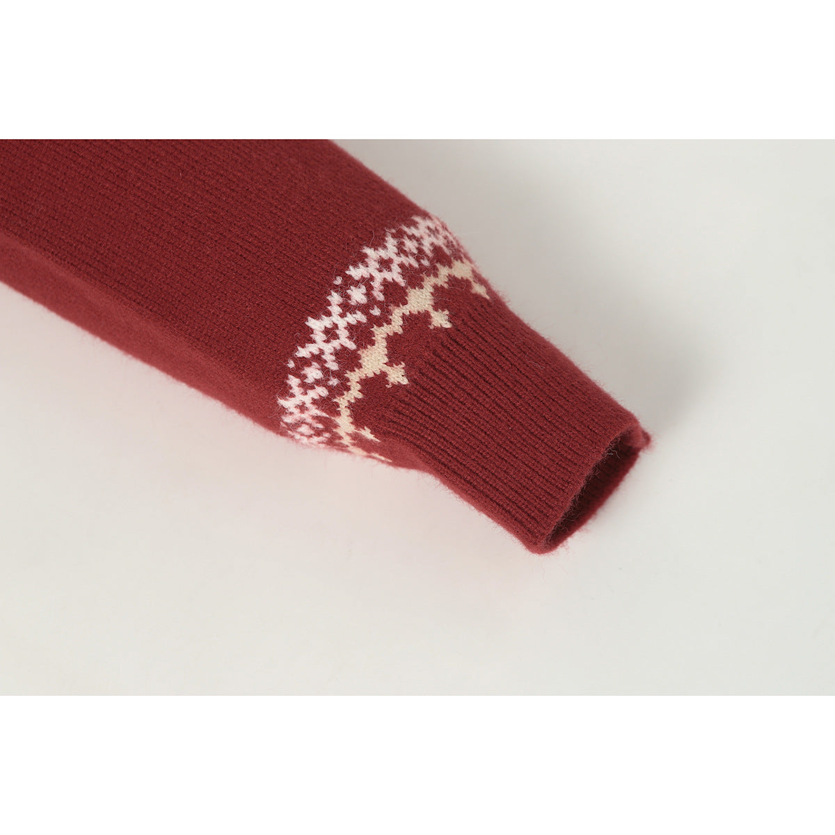 Close-up of a burgundy sweater sleeve and ribbed cuff with a cream geometric pattern band.