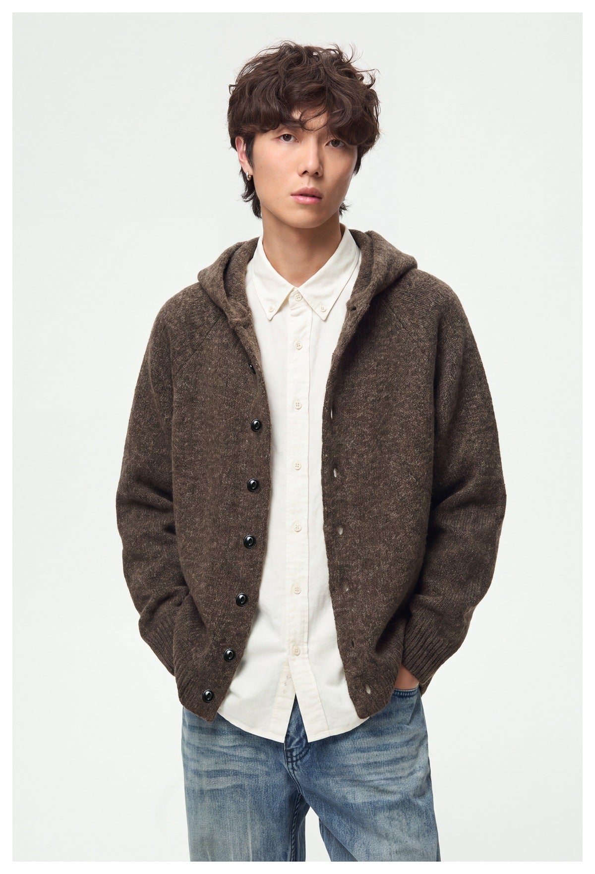 Model wearing a brown knit hooded cardigan with black buttons over a white shirt and blue jeans.