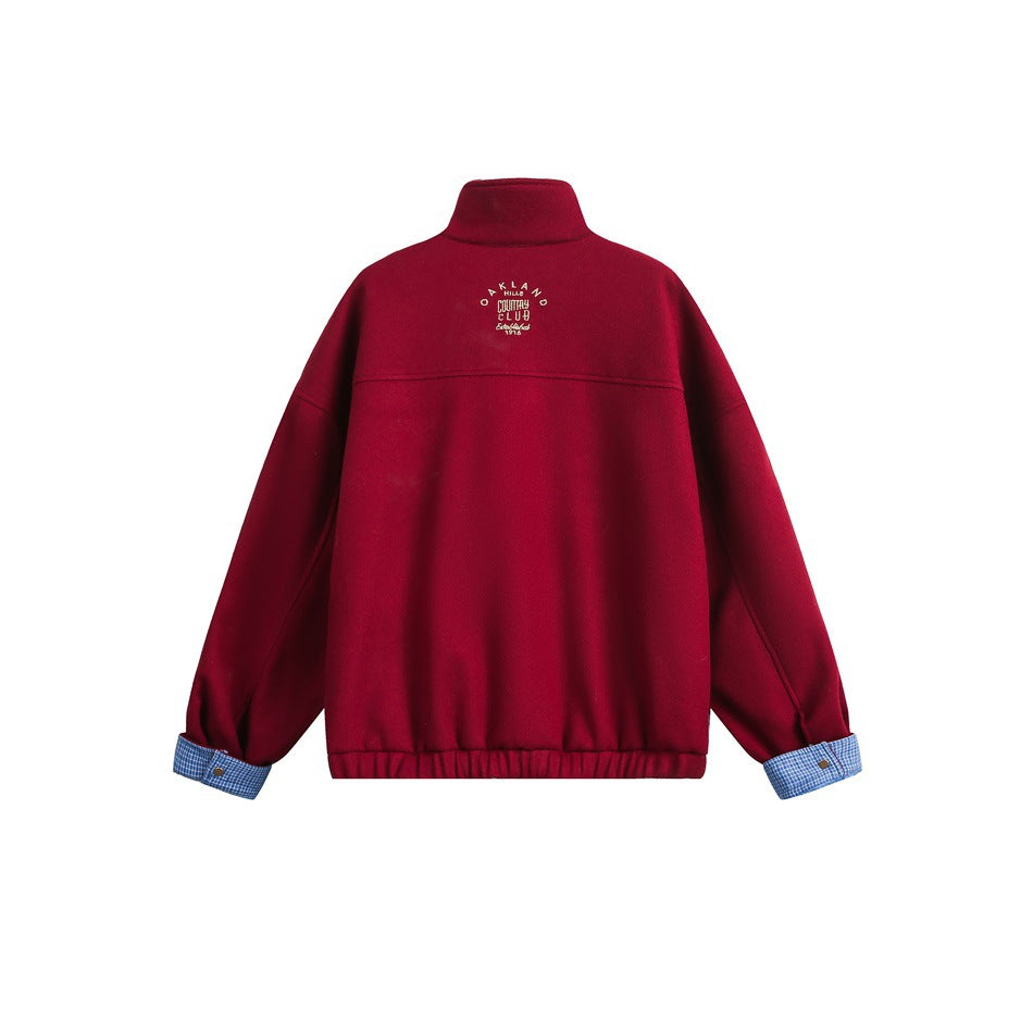 Back view of a red jacket with a high collar, gathered hem, blue checked turned-up cuffs and small embroidered text.