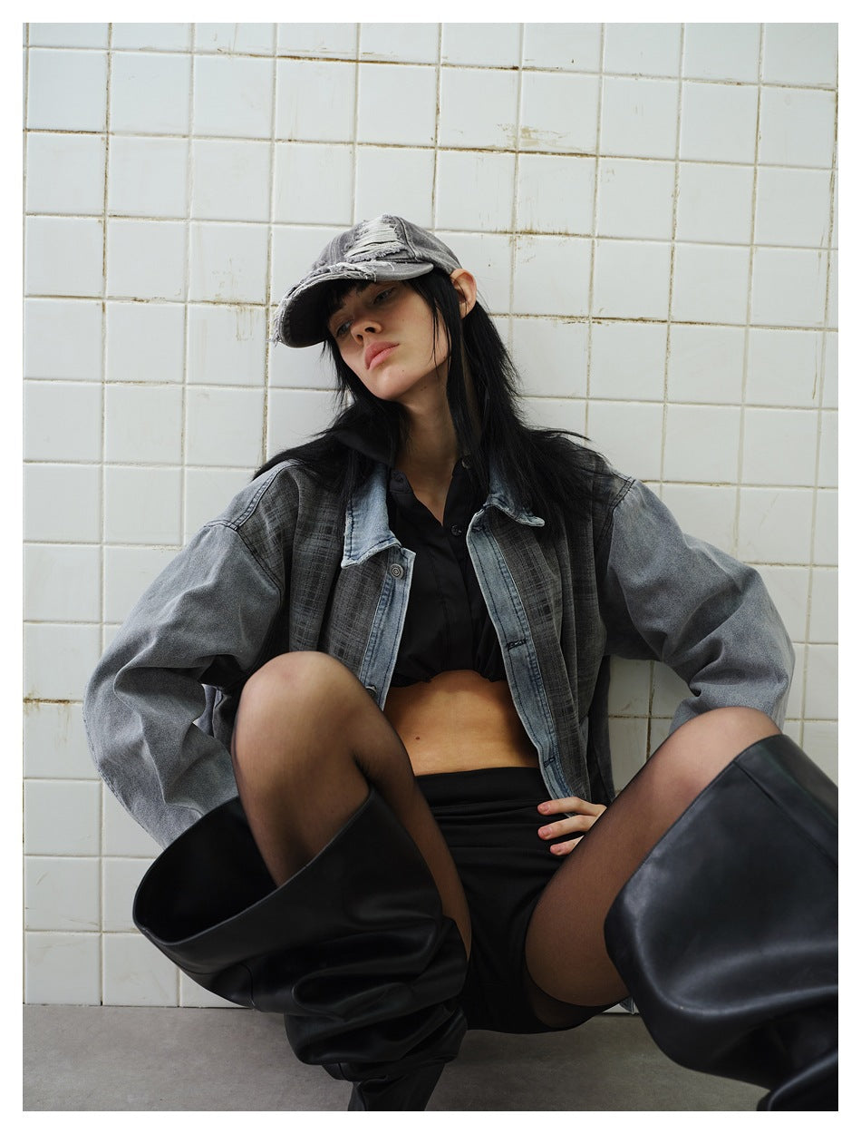 Seated model wearing an open charcoal plaid jacket with light blue denim trim and oversized gray sleeves.