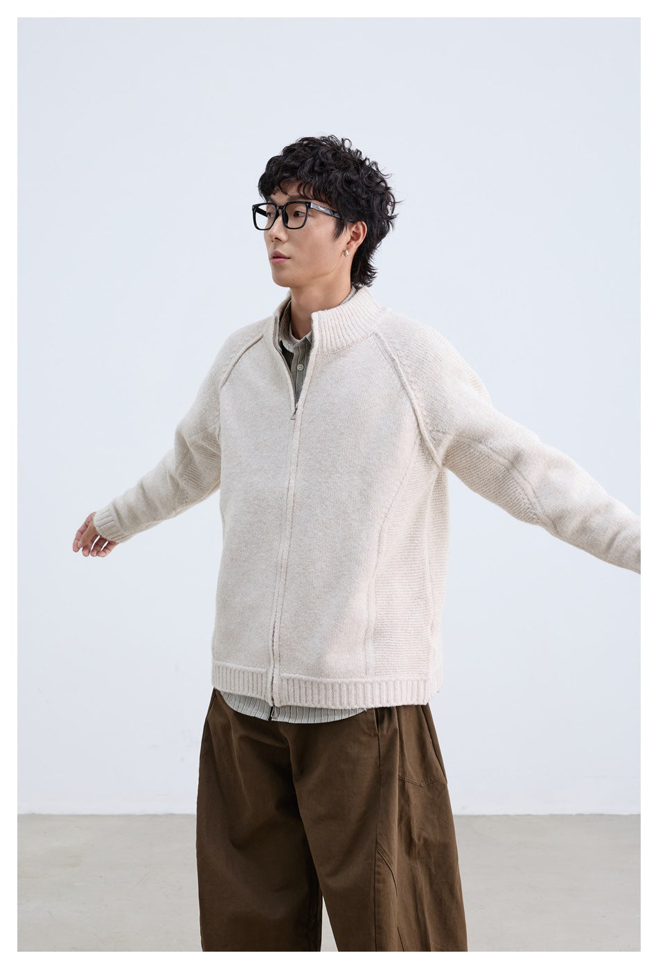 Model with arms outstretched wearing apricot zip-up knit cardigan with brown trousers, angled view