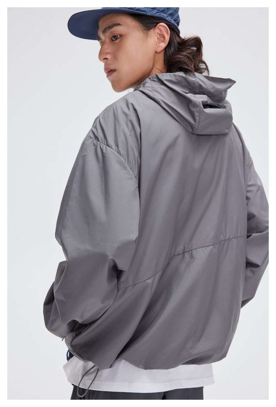 Model shown from behind wearing a gray hooded jacket and a blue cap.