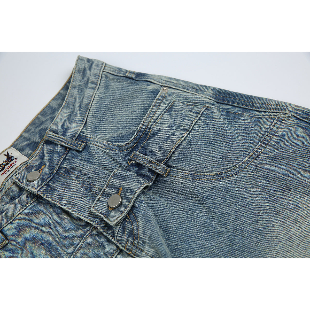 Close-up of light blue washed jeans showing the front pockets, waistband, belt loops, and button fly.