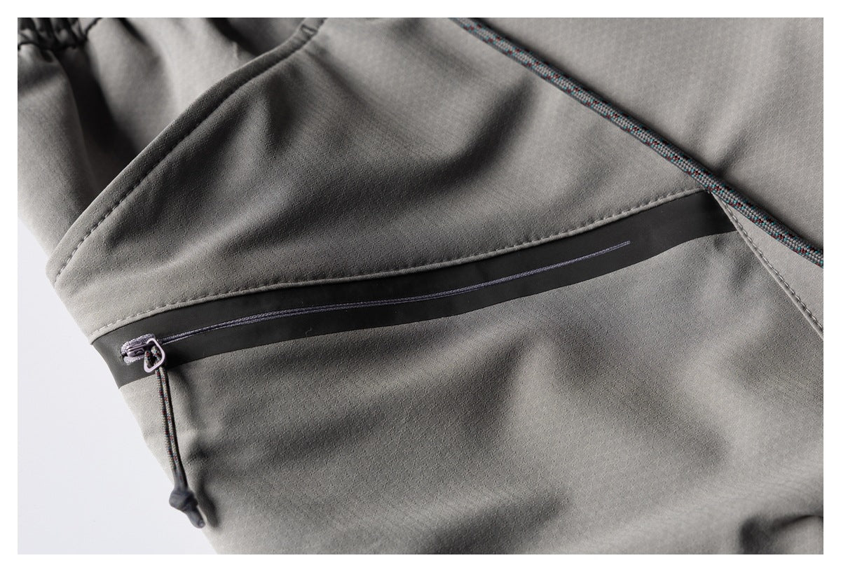 Close-up of gray trousers with a black-trimmed zip pocket and multicolored drawcord.