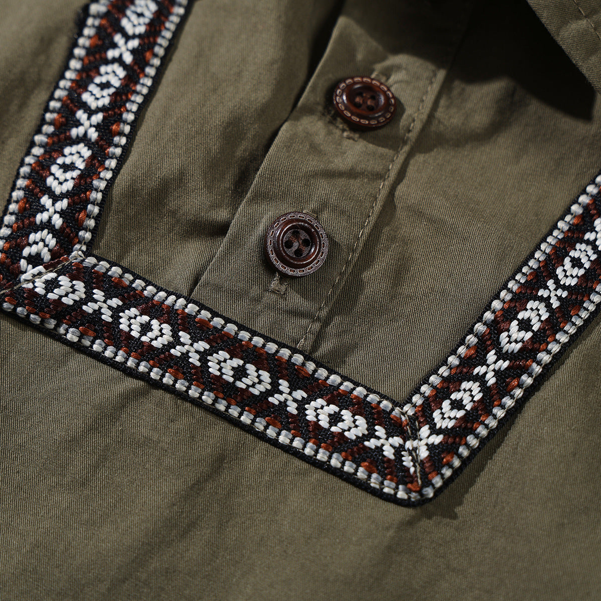 Close-up of an olive shirt's button placket and black, white, and rust geometric trim.