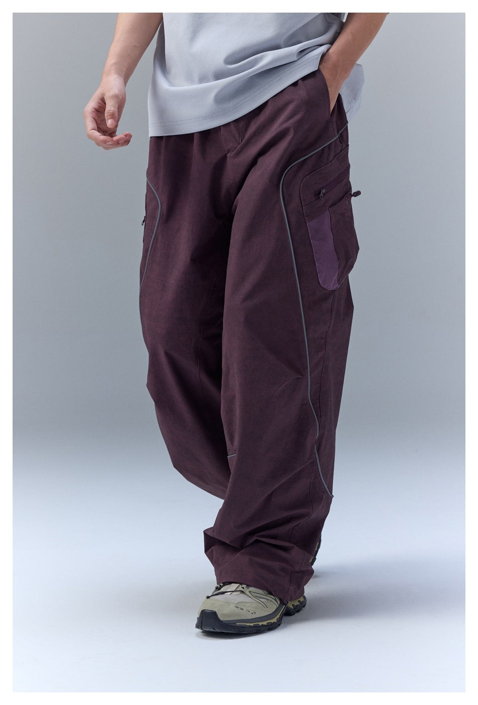 Close view of plum cargo trousers showing a large side pocket, zipper details, and curved contrast piping.