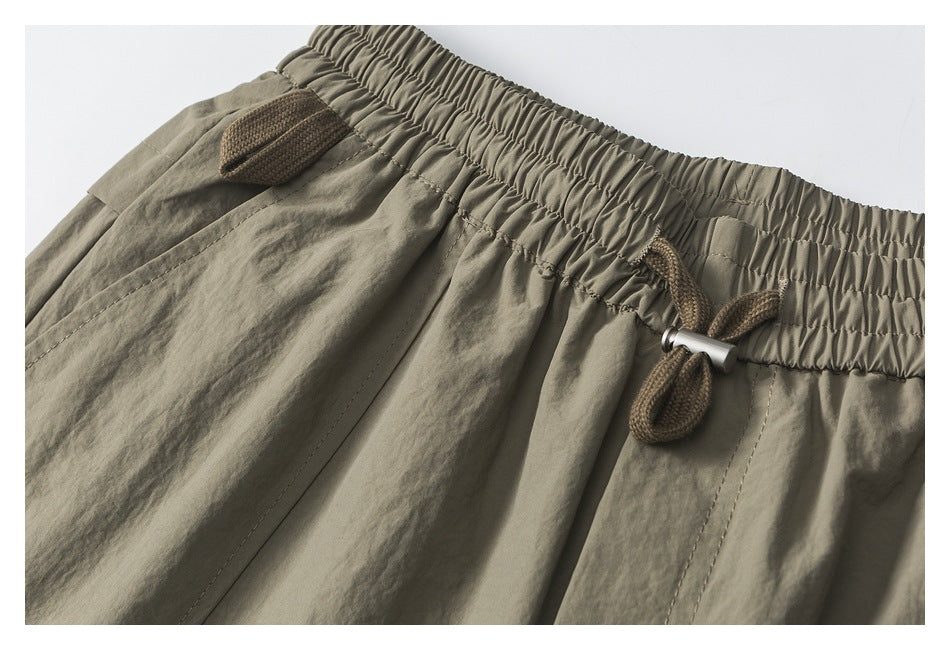 Close-up of khaki shorts with an elastic waistband, brown drawcord, and stitched pocket details.