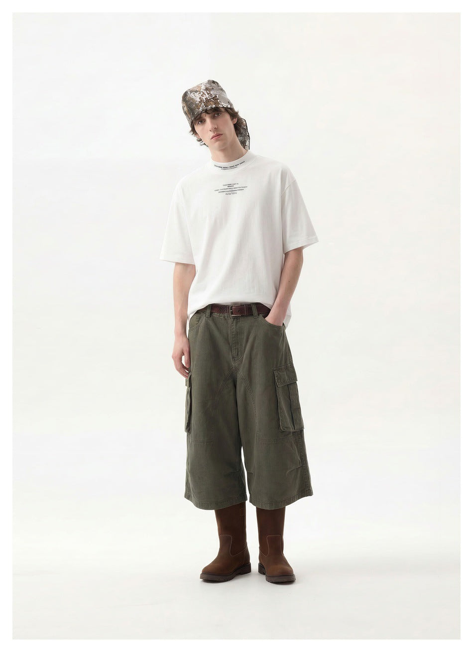 Full-length model wearing a white printed T-shirt, olive cargo shorts, brown boots, and a camouflage headscarf.