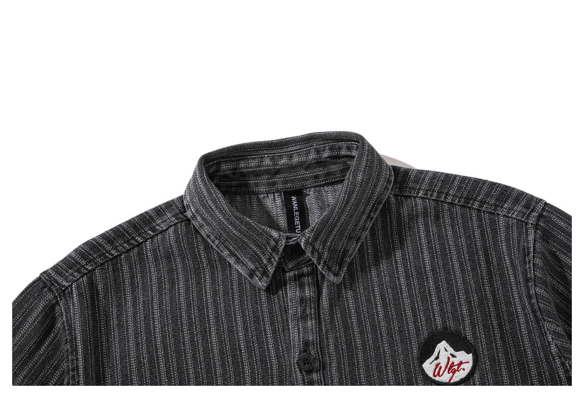 Close-up of a charcoal pinstriped button-up shirt showing its pointed collar, buttons and embroidered chest patch.