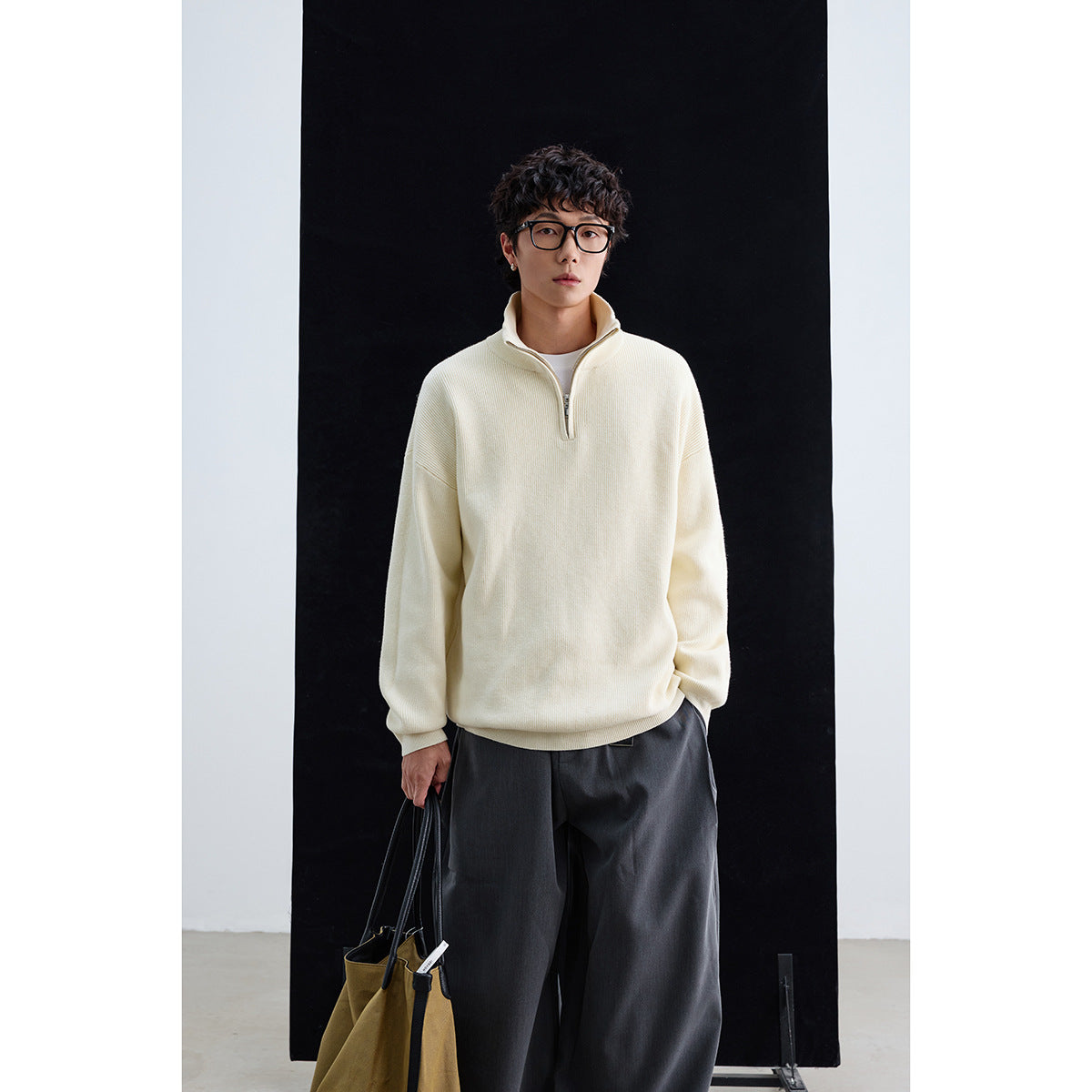 Model wearing an ivory high-collar quarter-zip pullover with dark trousers.