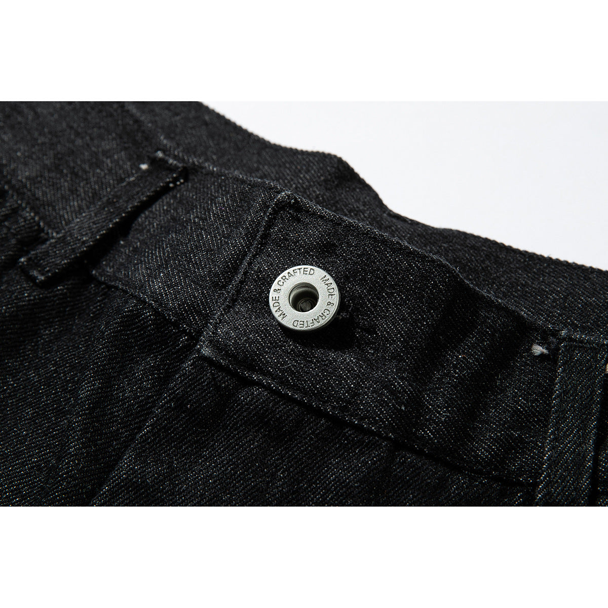 Close-up of black denim waistband with a silver snap button embossed with English lettering.