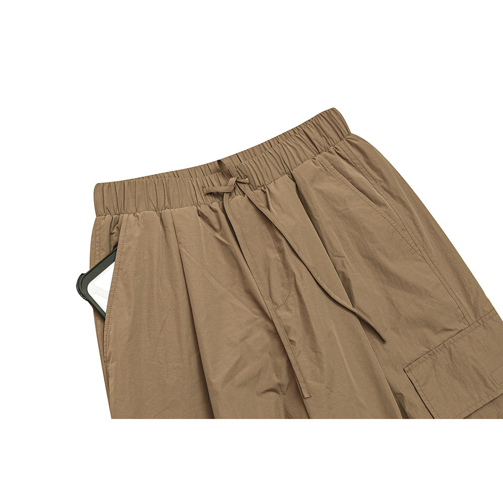Close view of tan wide-leg trousers with an elastic waistband, drawstring, front pockets and a cargo pocket.