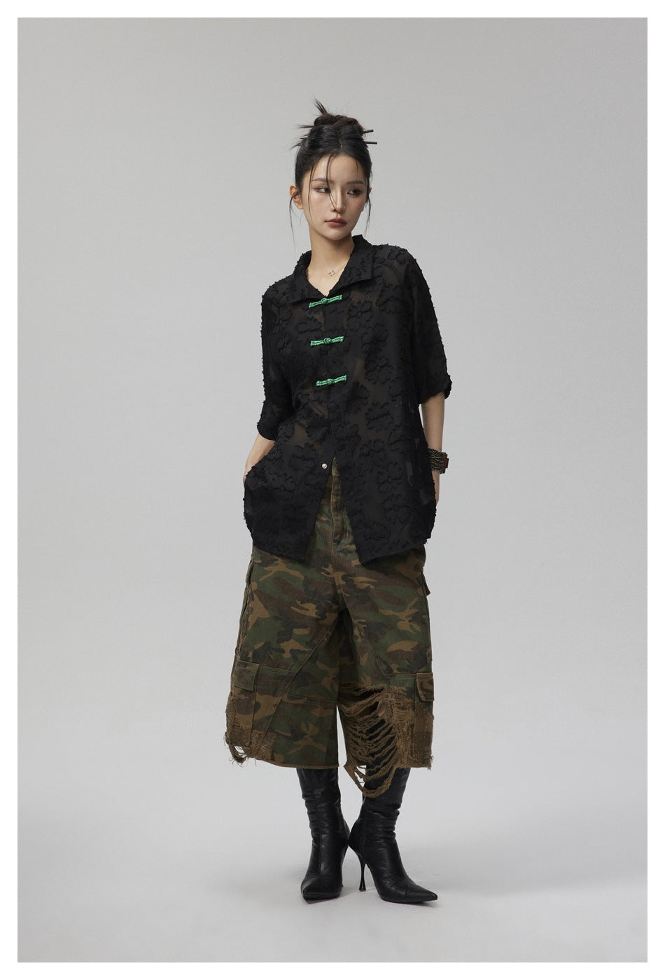 Model wearing black semi-sheer floral-textured short-sleeve shirt with green closures, camouflage shorts and black boots