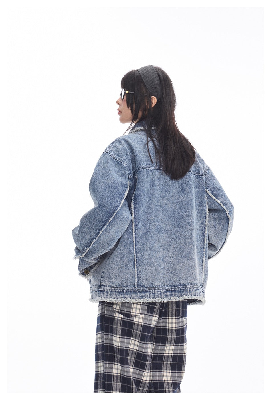 Rear view of a model wearing an oversized faded blue denim jacket with frayed seams and hem.