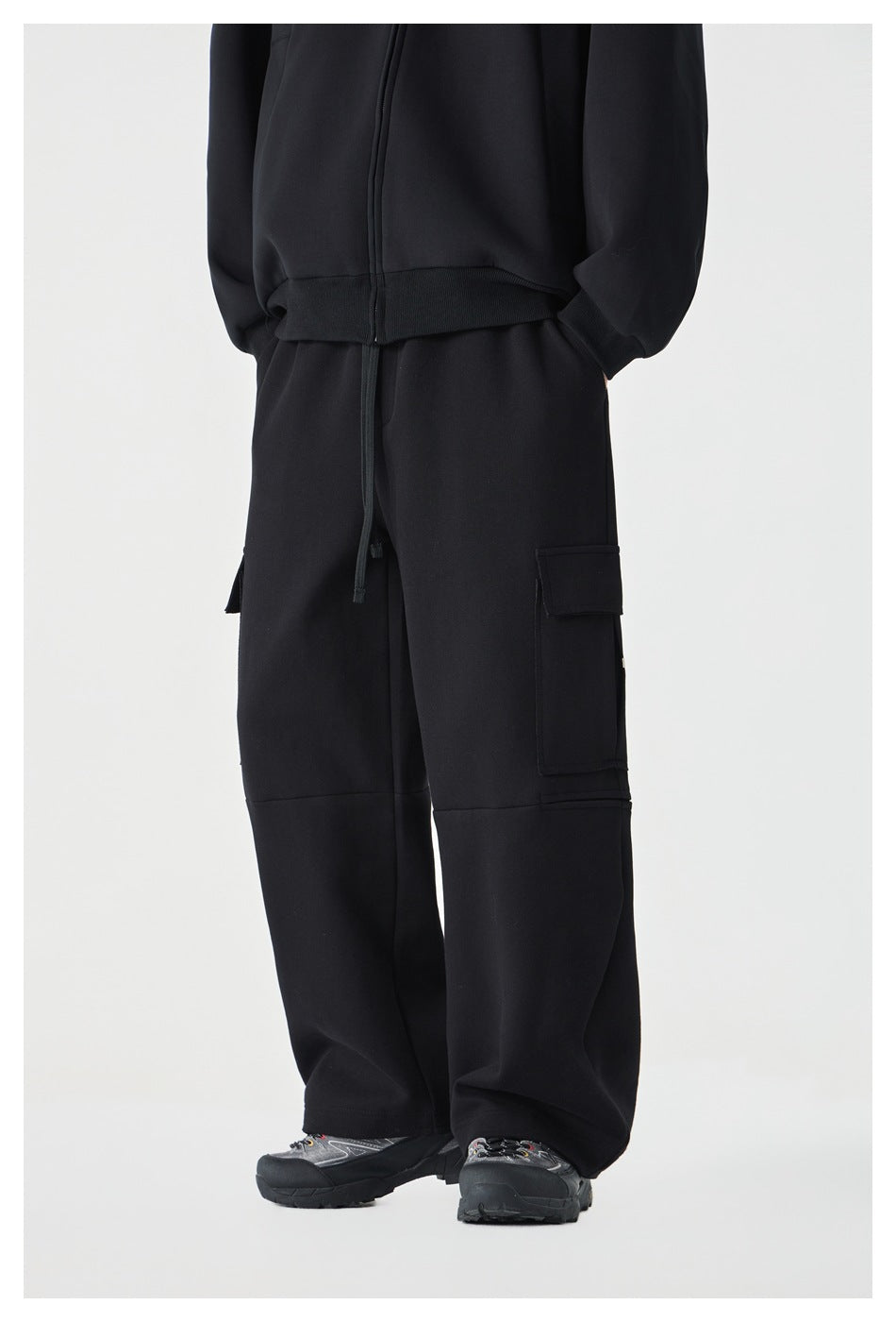 Cropped model wearing black wide-leg cargo pants with flap pockets and panel seams, viewed from the front at an angle.