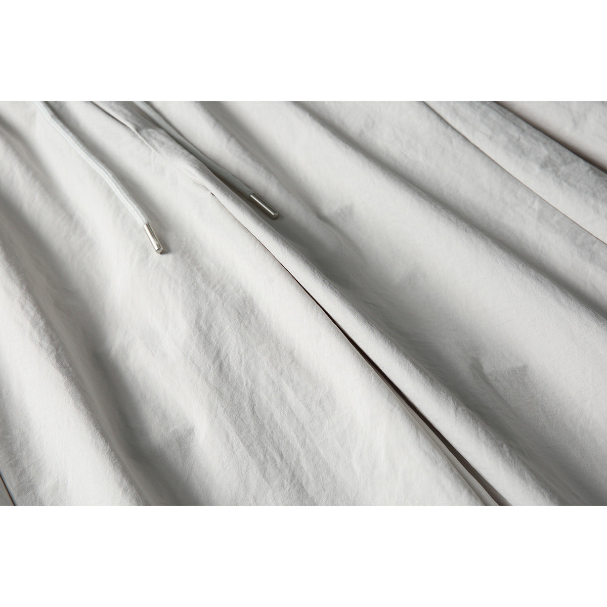 Close-up of light gray pants showing drawstring ends with metal tips and the front seam.