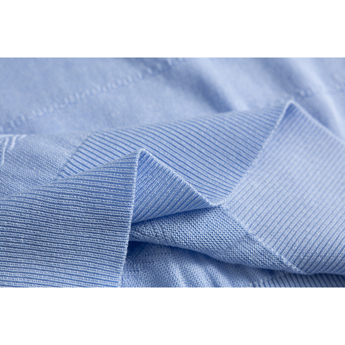 Macro view of light blue knit fabric with a folded ribbed edge and textured stitch patterns.