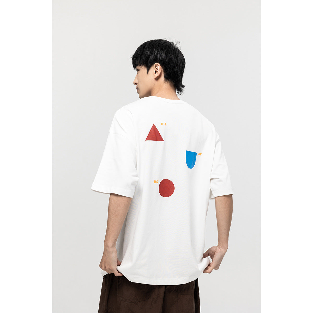 Back view of a model wearing a white oversized T-shirt with red and blue geometric graphics and small orange text.