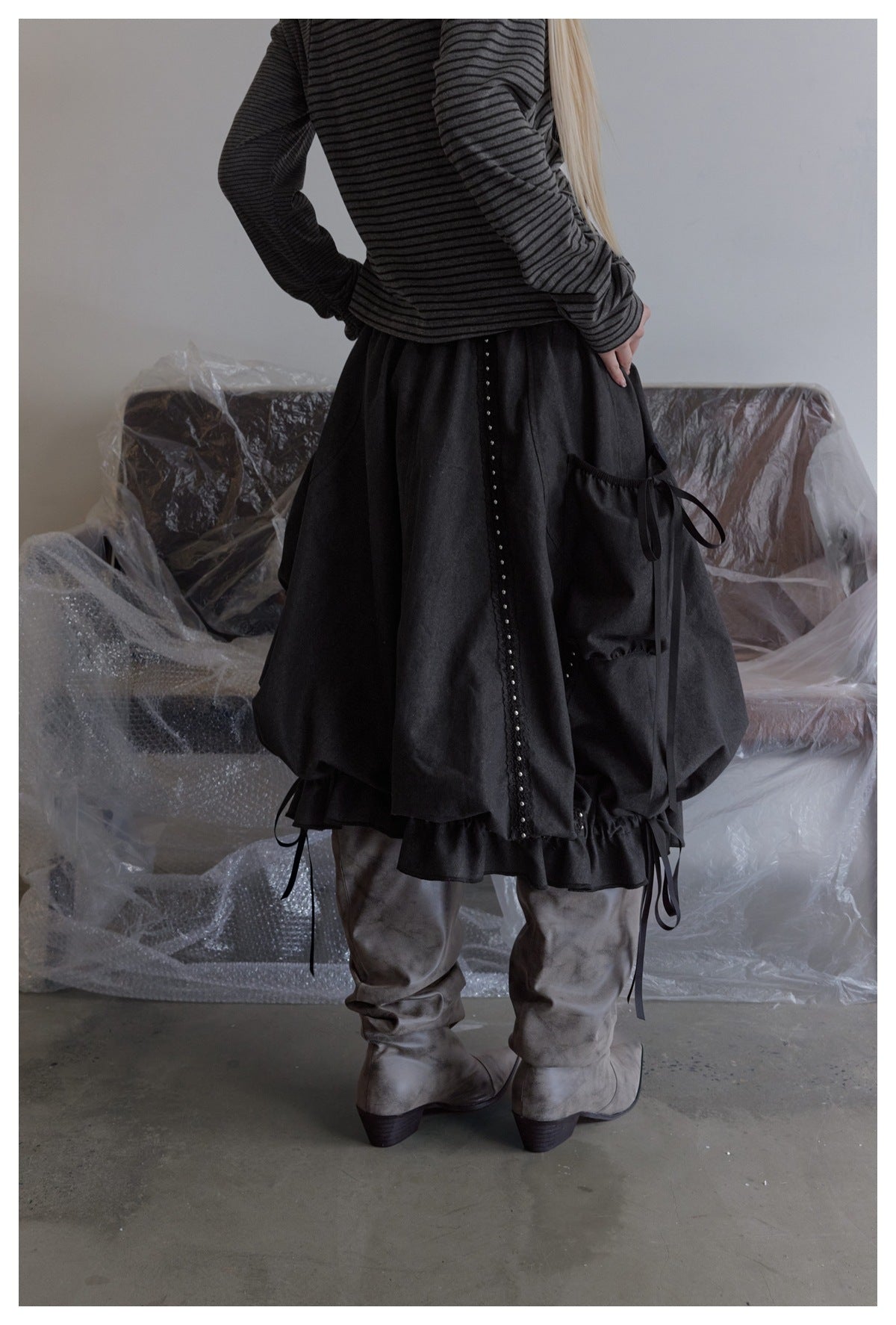 Rear view of a model wearing a charcoal gathered skirt with studded trim, a side pocket, and long ties.