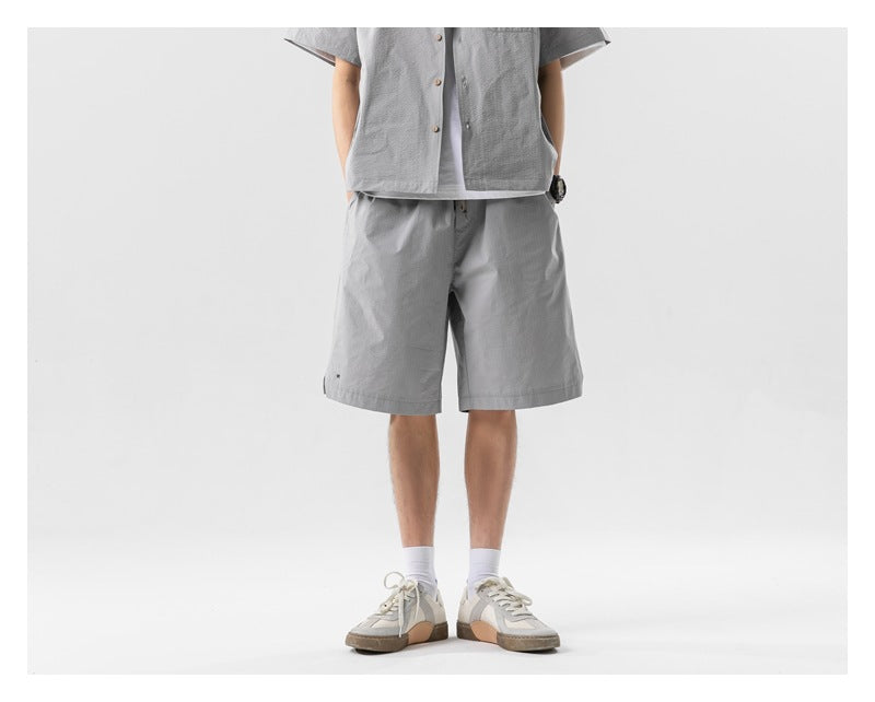 Person wearing gray relaxed knee-length shorts with a matching short-sleeve shirt and sneakers, front view cropped at the