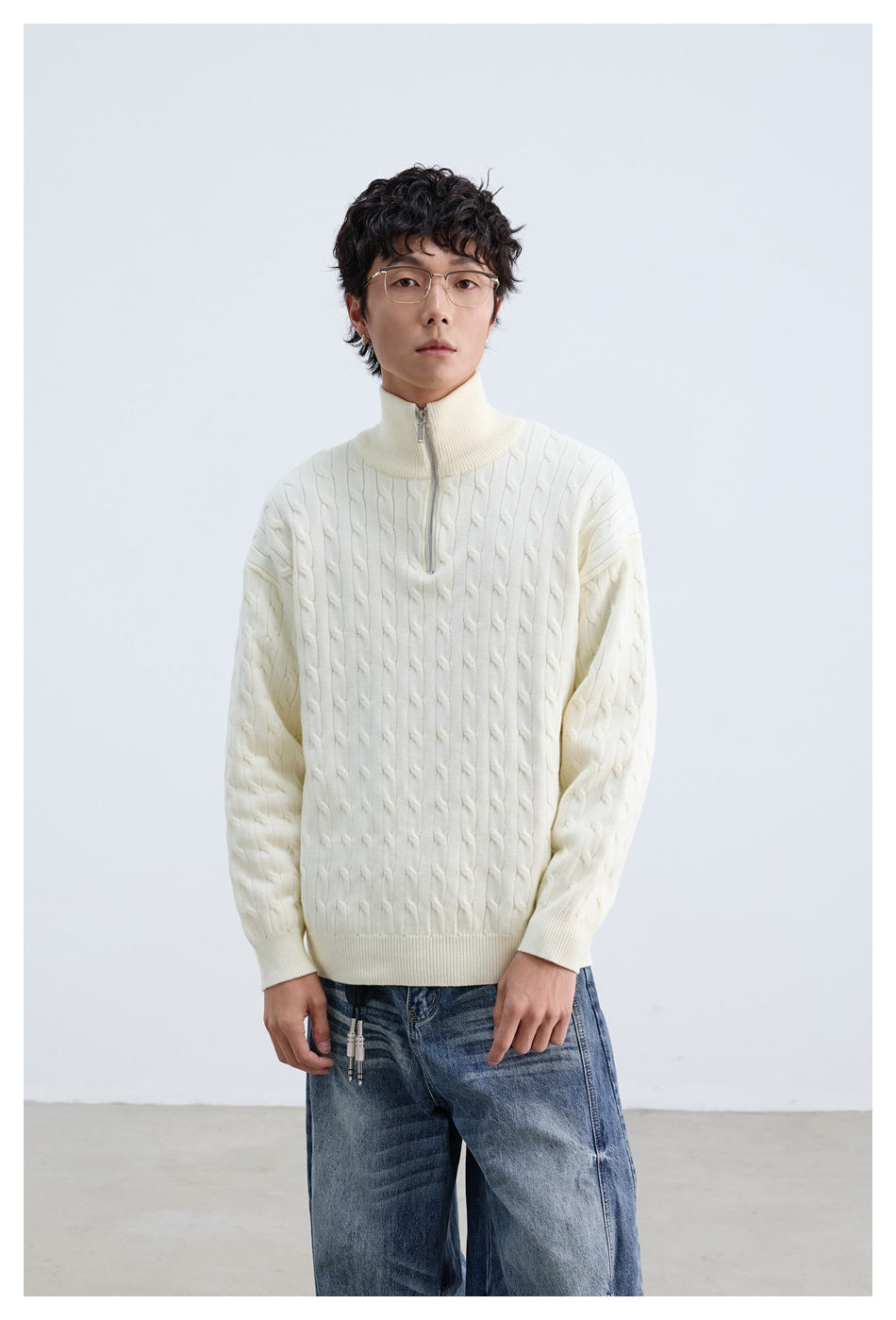 Front view of a model wearing an ivory cable-knit quarter-zip sweater with a ribbed raised collar.