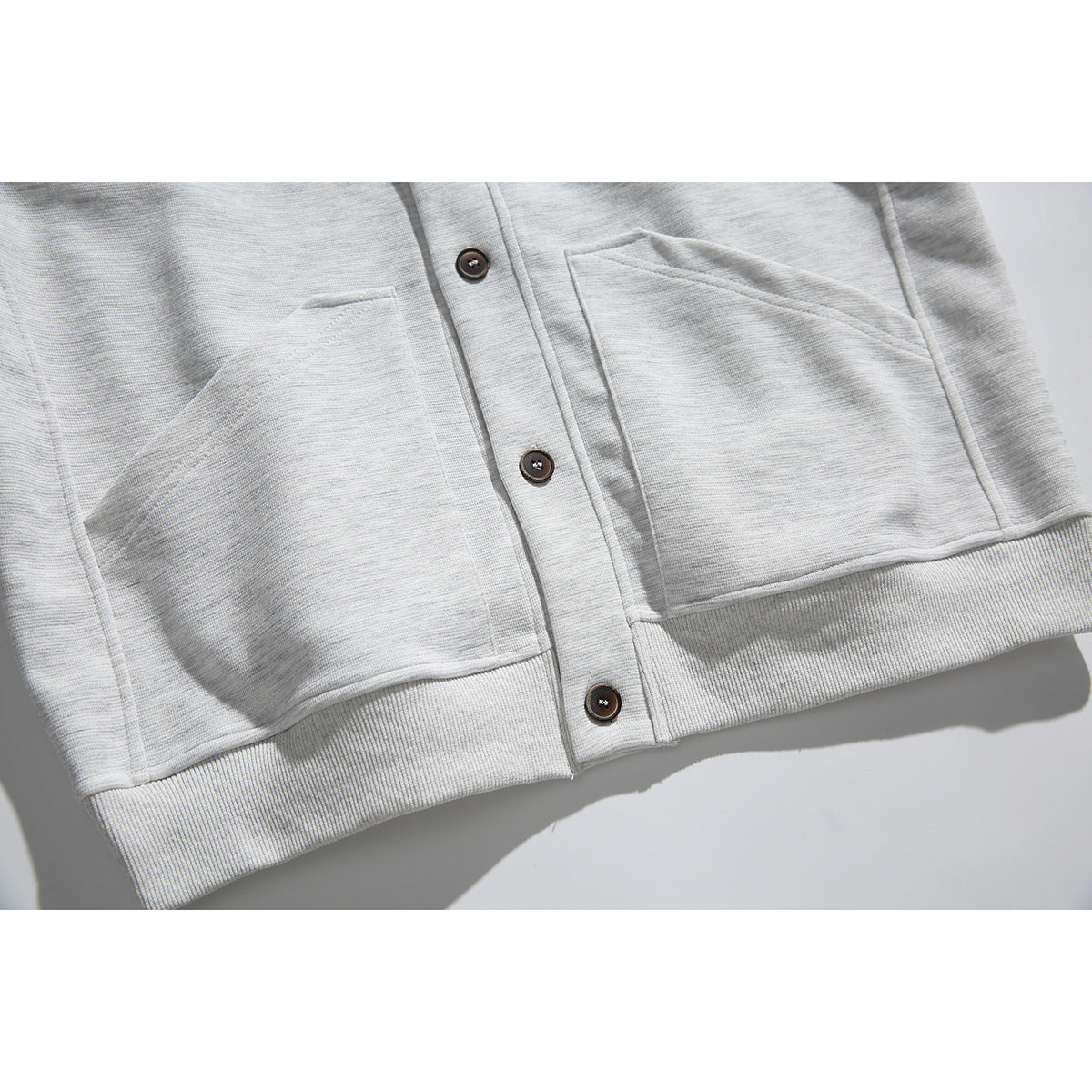Close-up of the cardigan’s two front patch pockets, dark buttons, and ribbed hem.