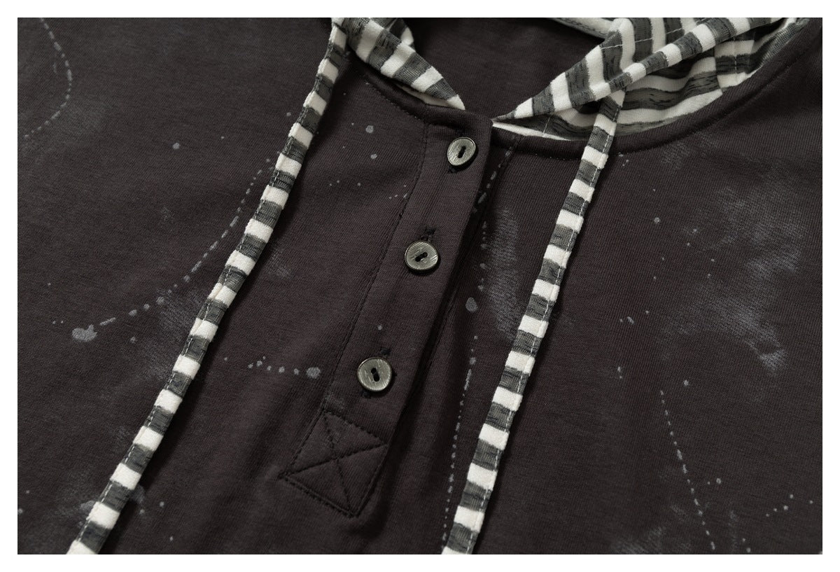 Close-up of a dark garment's button placket, striped drawstrings, and pale scattered markings.