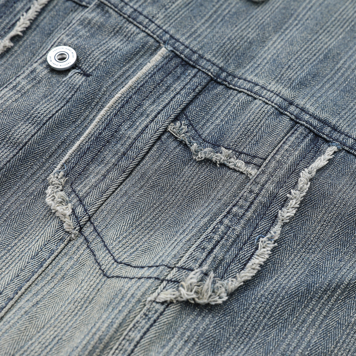 Close-up of a blue-gray denim jacket pocket with frayed edges, visible stitching, and a metal button.