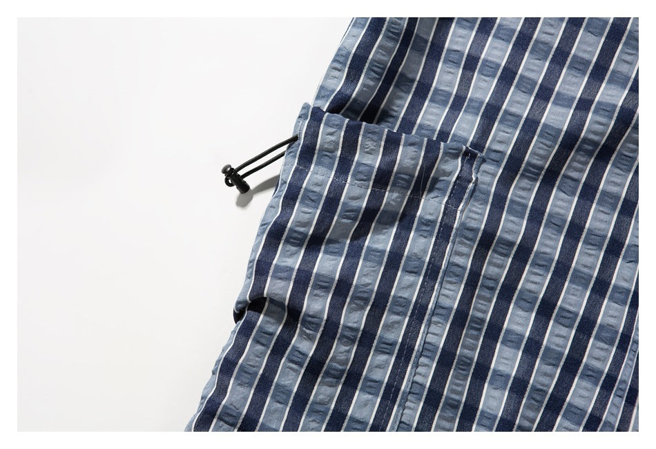 Close-up of blue-gray striped shorts showing a black side drawcord and stitched fabric details.