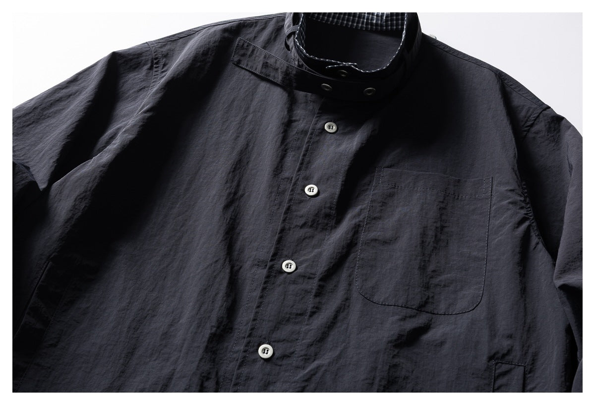 Close view of a dark charcoal button-up shirt with a stand collar, pale buttons, and a large chest pocket.