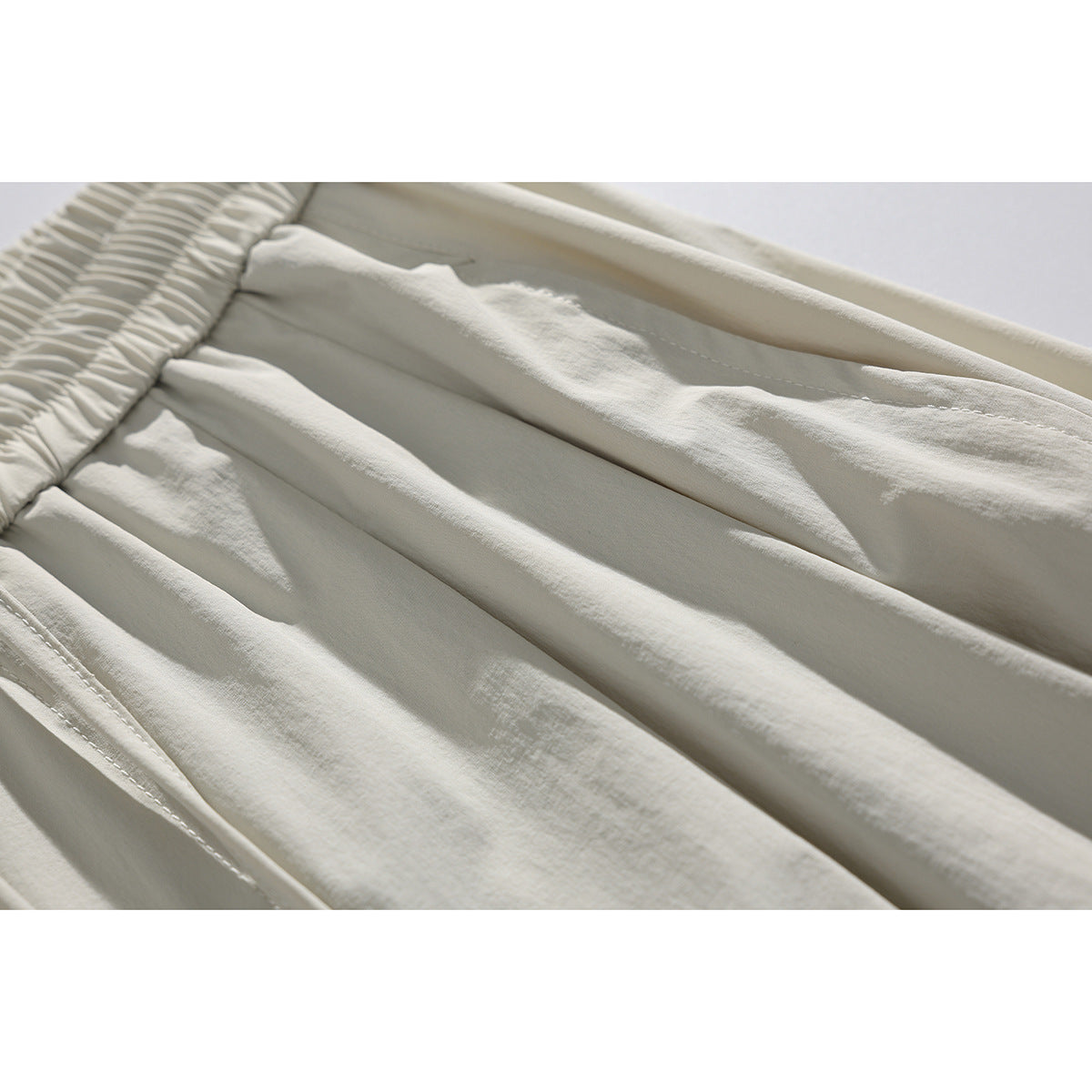 Close-up of light beige shorts showing the gathered elastic waistband, seams, and fabric texture.