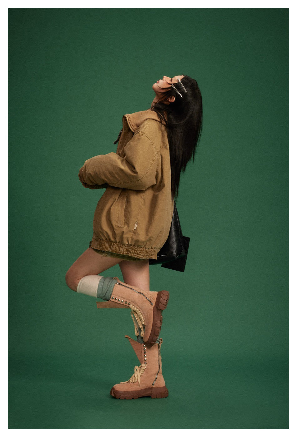 Side view of model in a tan oversized jacket with elastic hem, posed against a green backdrop