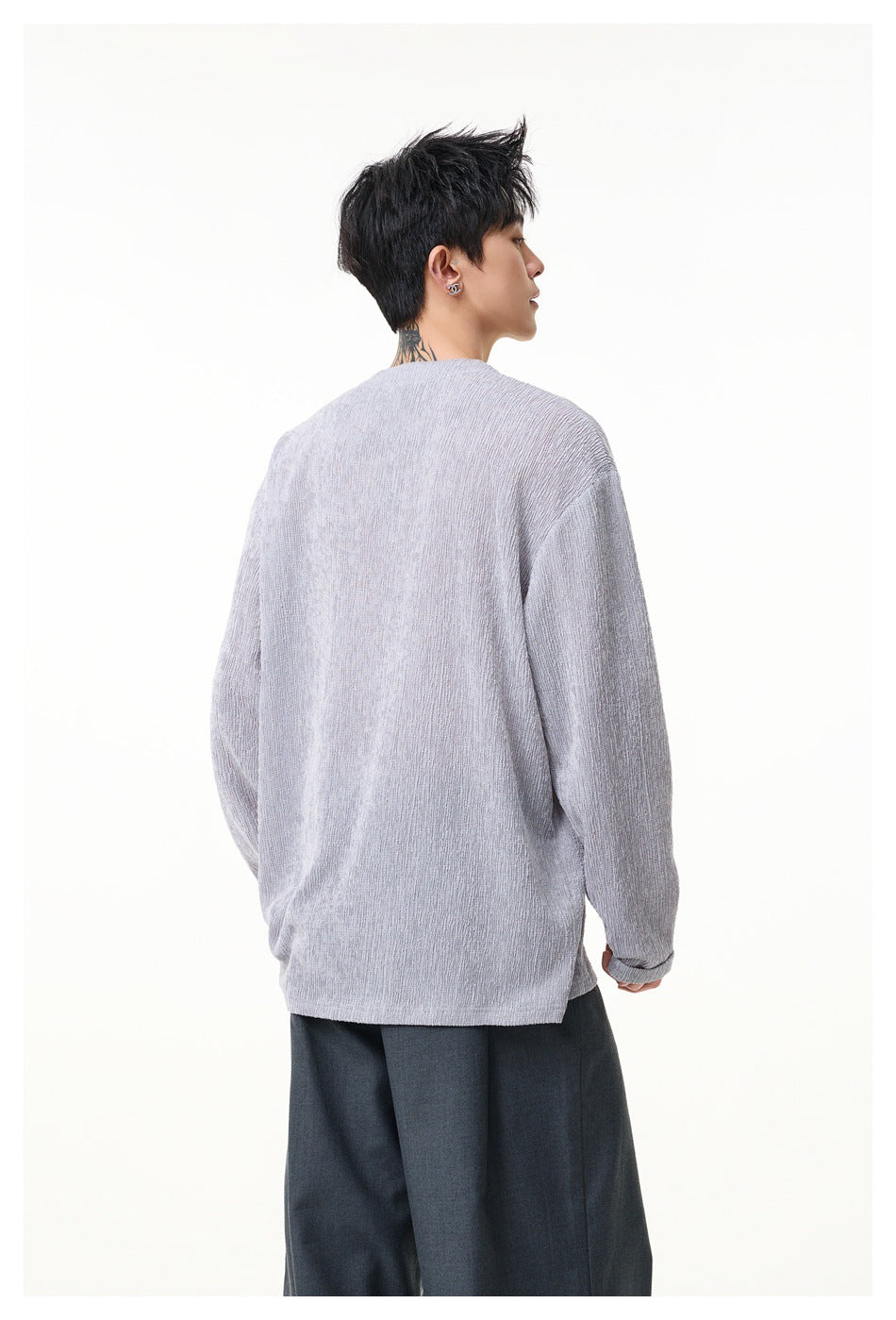 Back view of a model wearing a light gray oversized long-sleeve henley with dark trousers.