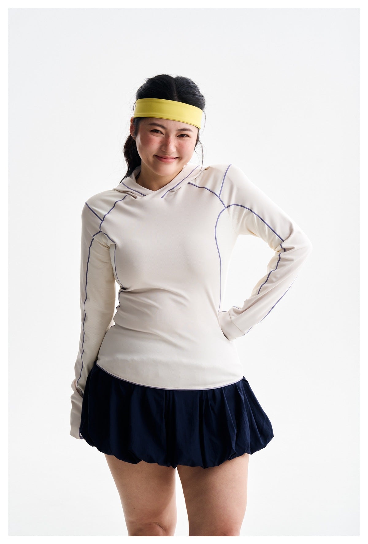 Model wearing an ivory hooded top with purple piping and a navy bubble skirt, shown from head to upper thighs.