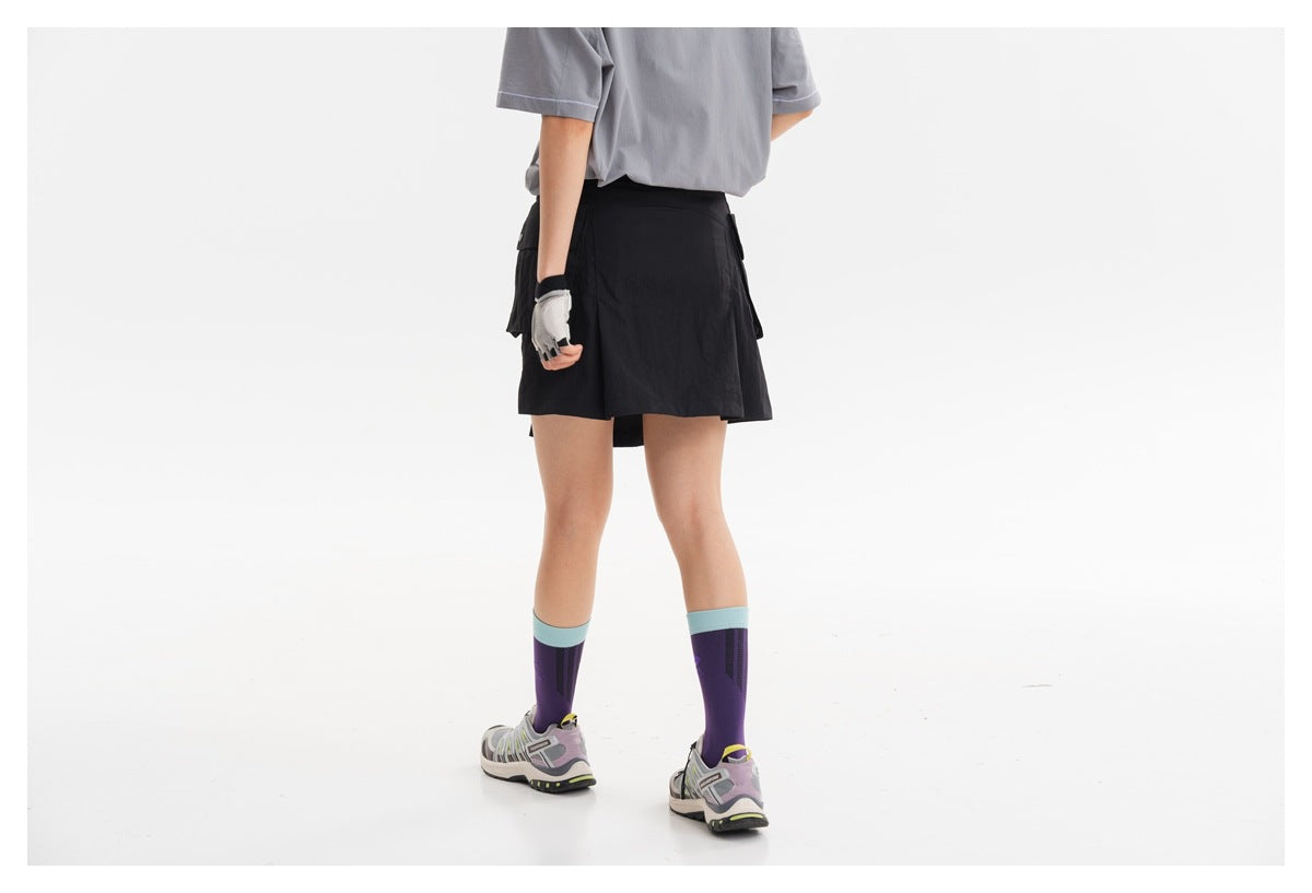 Rear view of a model wearing a black short skirt with side flap pockets and a gray T-shirt.