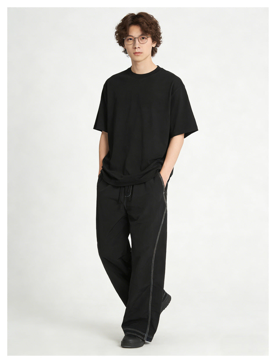 Model wearing black wide-leg pants with white contrast stitching and a black T-shirt.