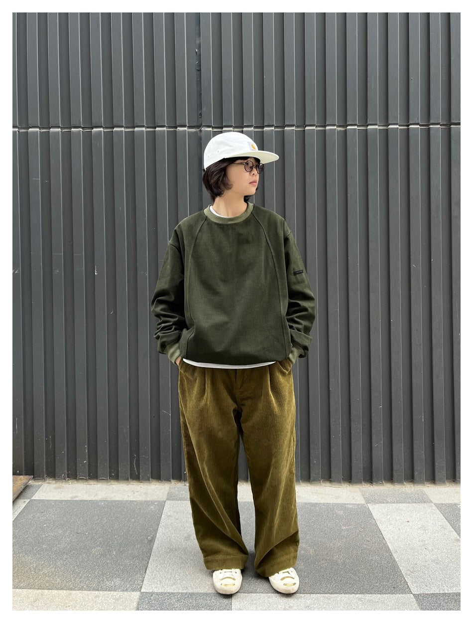 Person wearing an olive crewneck sweatshirt with raglan sleeves and wide-leg olive-brown trousers.