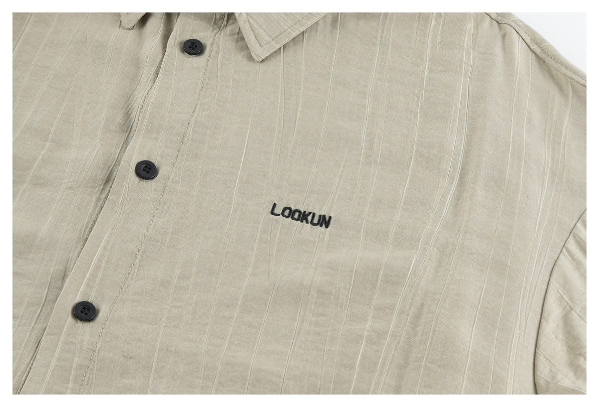 Close-up of the beige shirt front with dark buttons, subtle vertical texture and small black embroidered lettering.