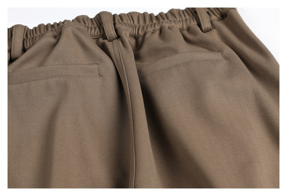 Close-up of taupe trousers with an elastic waistband, belt loops, drawstring, and rear welt pockets.