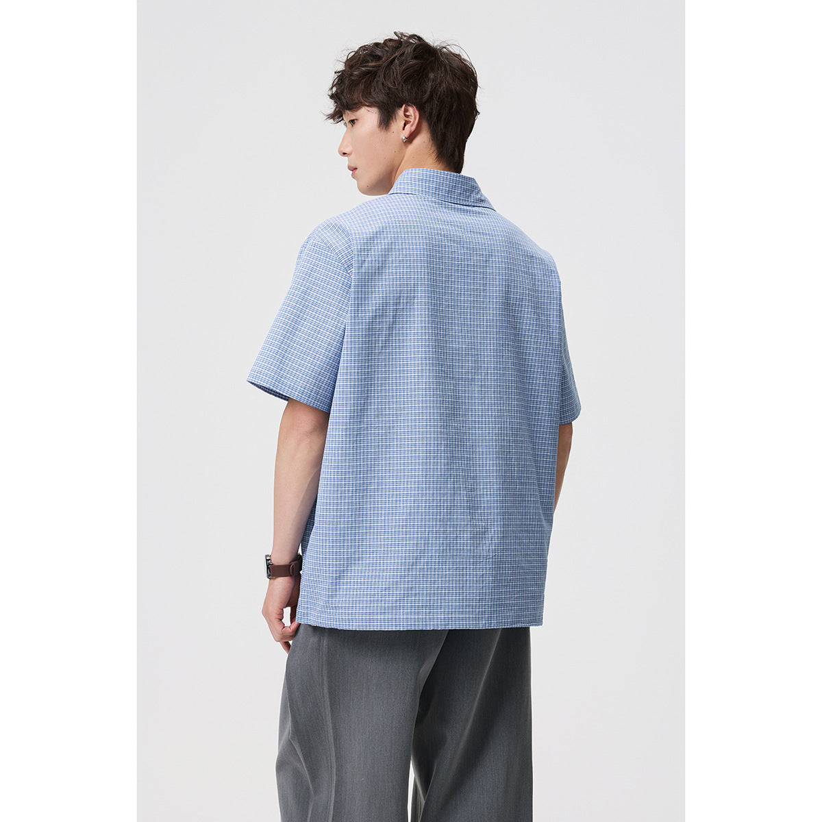 Back view of a man wearing a blue-and-white micro-check short-sleeve collared shirt.
