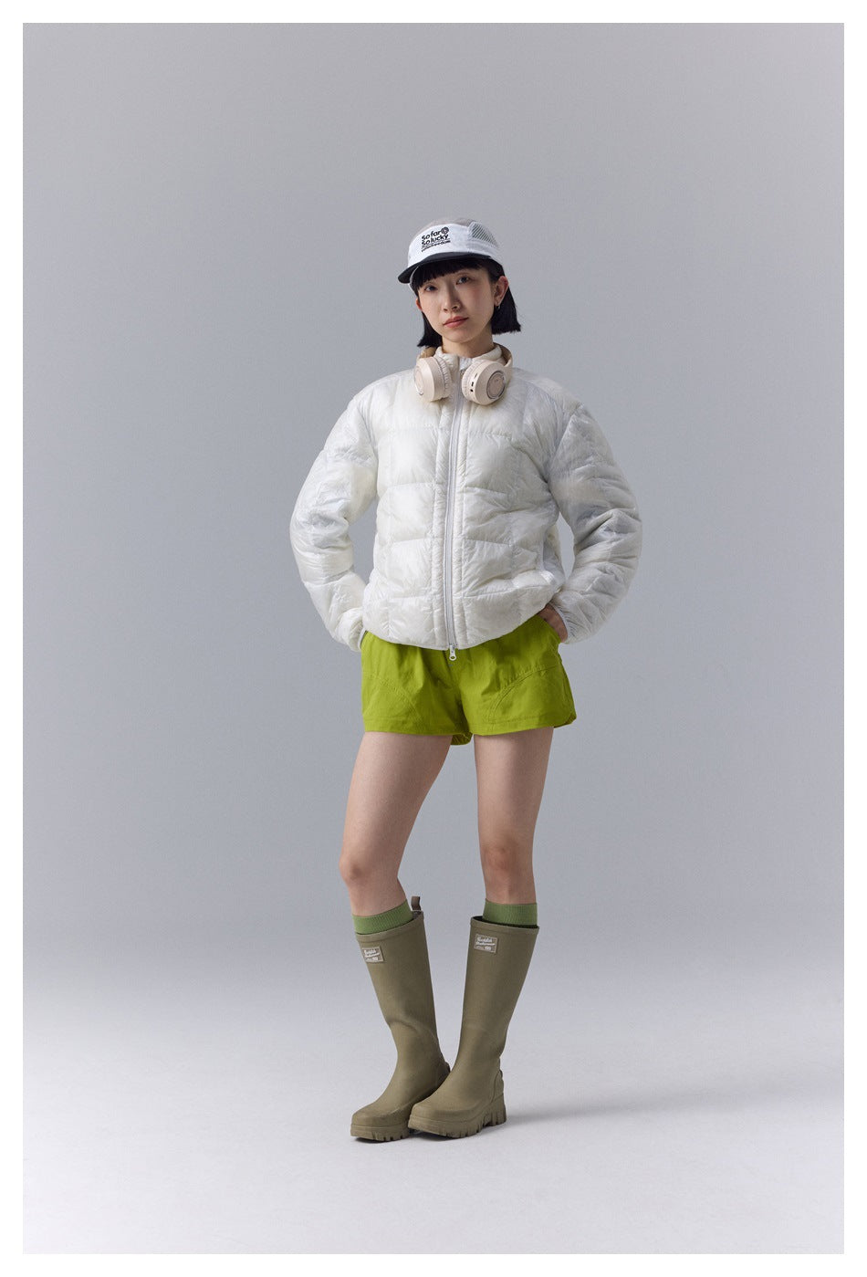 Model wearing a white quilted zip jacket with bright green shorts and olive knee-high boots.