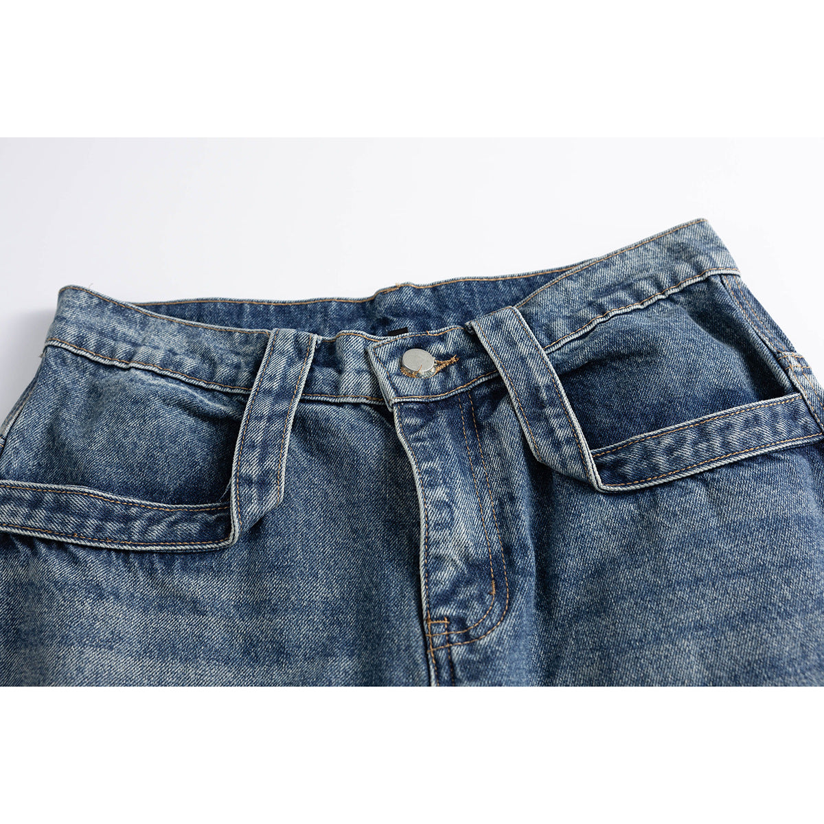 Close-up of blue distressed denim jeans showing the buttoned waistband, belt loops and large angular front pockets.