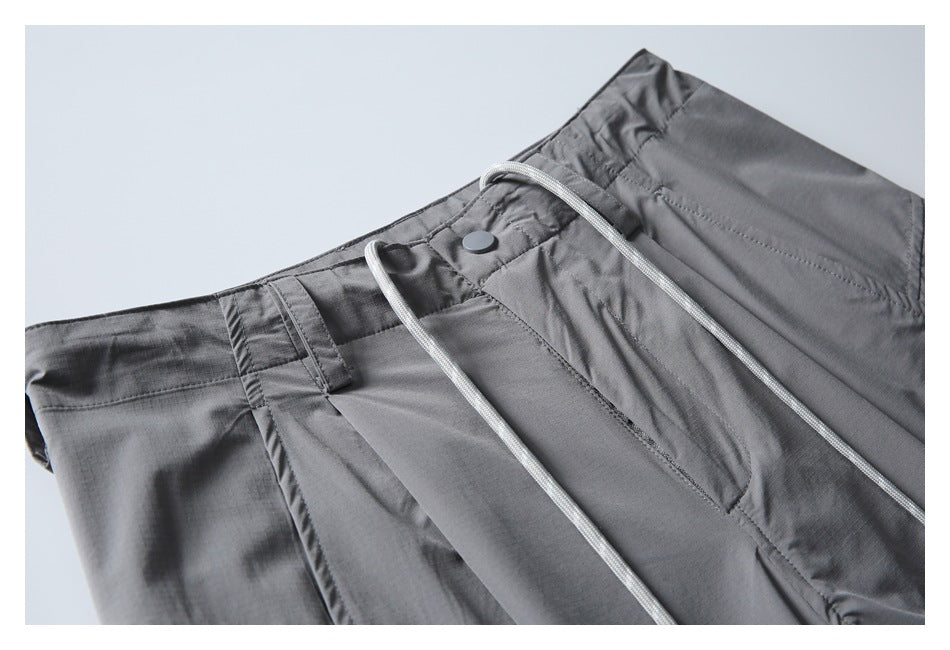 Close-up of gray pants showing the waistband, snap closure, white drawcord, and pocket stitching.