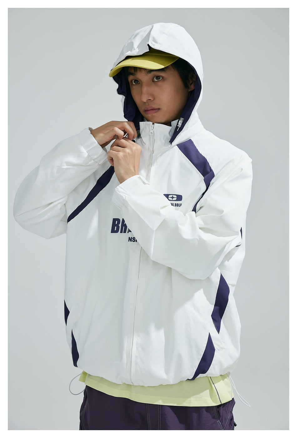 Model adjusting the collar of a white hooded jacket with navy panels and printed English lettering.