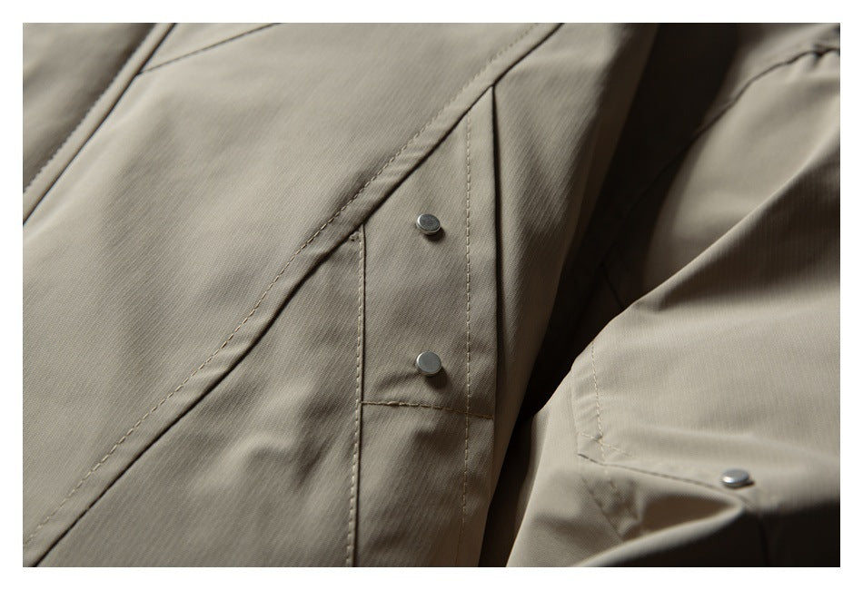 Close-up of a taupe jacket front with a stitched snap-button tab and part of the sleeve.